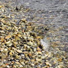 Background of sandy, stones and flowing waves on the sea beach. Summer holidays concept