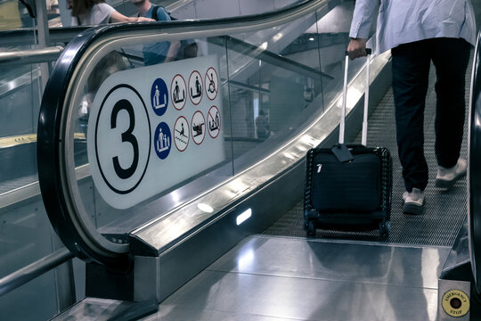 tourist with travel luggage steps on travelator, tread or moving walkway in airport terminal, emergency stop button