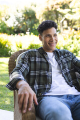 Portrait of happy biracial man sitting in chair in sunny garden, copy space