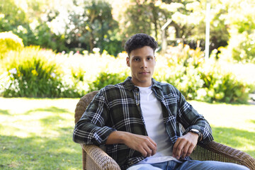 Portrait of focused biracial man sitting in chair in sunny garden, copy space