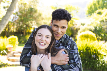 Portrait of happy diverse couple embracing in sunny garden, copy space