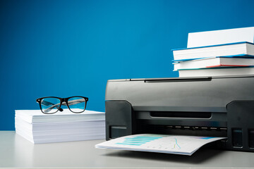 Laser printer on desk against blue background.