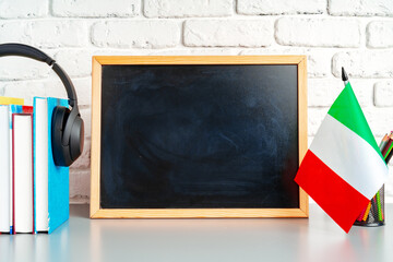Stack of books, blackboard and flag of Italy on desk. Italian language learning concept