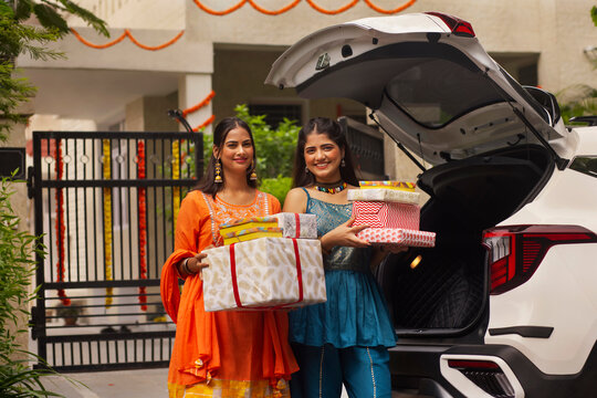 Two sisters unloading Diwali gifts from car trunk after shopping