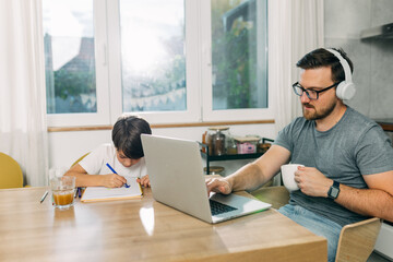 Working father is answering mails on laptop while his son is drawing next to him.