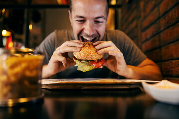 A hungry man is eating tasty and delicious hamburger at fast food restaurant.