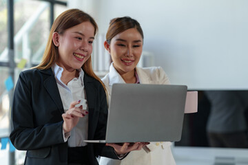 Two Asian businesswomen come up with an idea. Discuss investment projects and strategic planning with information via various documents and files. On a laptop computer at modern office.
