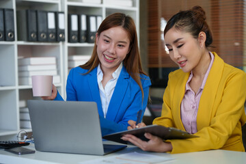 Obraz premium Two Asian businesswomen come up with an idea. Discuss investment projects and strategic planning with information via various documents and files. On a laptop computer at modern office.
