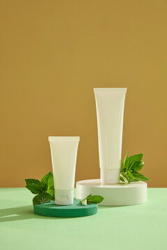 Advertising photo for cosmetic with spearmint extract. Set of cosmetic tubes mockup on podiums with spearmint leaves on yellow background. Spearmint is a minty herb that’s high in antioxidants