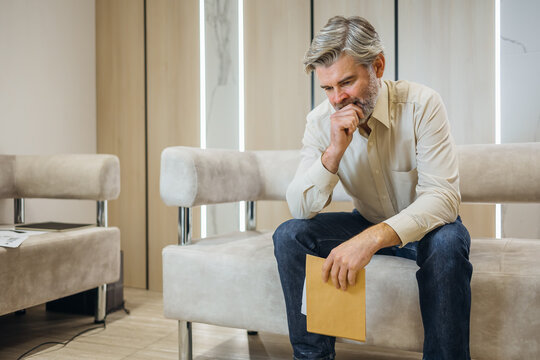 unhappy young man opening envelope with letter about financial problem bank medical result sitting on couch in living room at home Upset male received bad new by mail failure refusal. diagnosis