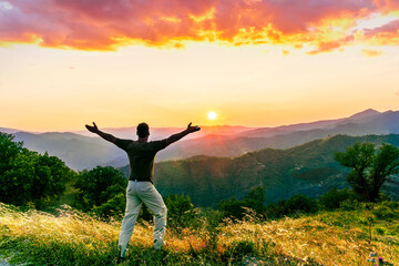 rejoicing man with beautiful scenic mountain sunset landscape on background. happy man watching amazing evening sunset