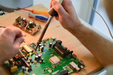 a master with a soldering iron soldering a chip, the concept of data, hardware, technician and...