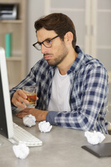 man holding alcoholic drink looking at laptop