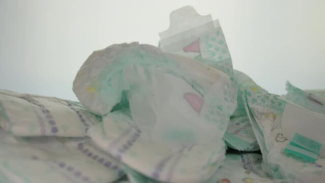 A baby diaper falls on a white background onto a pile of scattered diapers. The concept of comfortable diapers, protection against leakage. children's hygiene. Slow motion