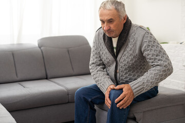 close up hands man with his knee joint pain in sofa, pain in the elderly, health care. Grandfather...