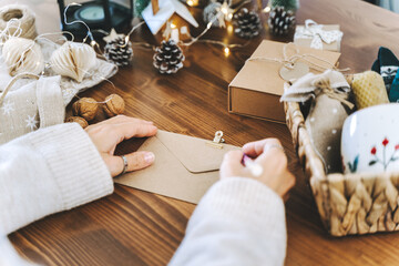 Woman s hands wrapping Christmas gift envelope, close up. Unprepared presents on white table with...