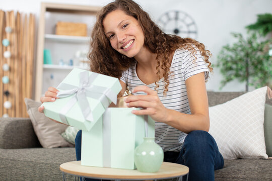 happy woman sitting on couch at home opening carton box