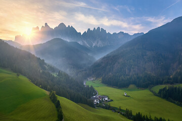Morning view of idyllic landscape of the Dolomites in Val di Funes, South Tyrol, Italian Alps. Aerial view of the   Santa Magdalena village, green meadows and steep rock peaks with rising sun.