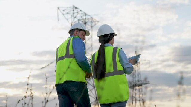 Engineer and trainee with tablet review power transmission at substation area