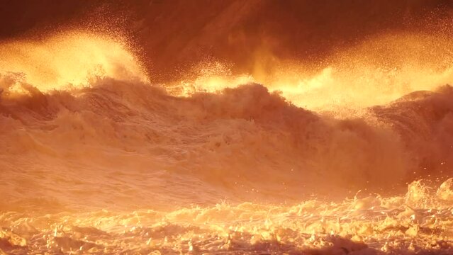 Storm Wave Sunset. Large wave crashing into shore, creating foam and spray at golden burning sunset. Seascape with storm breaking waves. Weather and climate change