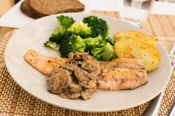 Fried river trout fillet with a complex side dish of broccoli, baked potatoes and mushroom sauce