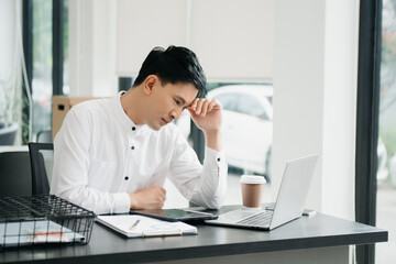Naklejka premium Frustrated young businessman working on a laptop computer sitting at his working place