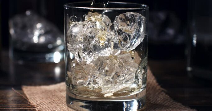 Super slow motion macro of bourbon whiskey poured by bartender in transparent glass with fresh cool ice while preparing an vodka cocktail at 1000 fps.