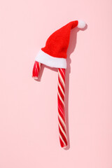 Christmas candy cane with Santa Claus hat on pink background, top view