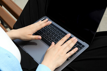 The girl works on a laptop while sitting on a bench