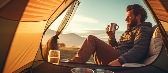 Young tourist man happily savoring freedom with coffee in the tent copy space image - obrazy, fototapety, plakaty