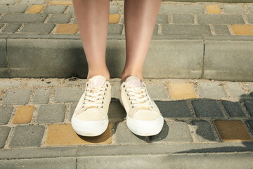 Stylish white sneakers on women's legs on cobblestones