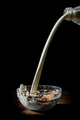 Corn flakes with flowing milk on black background