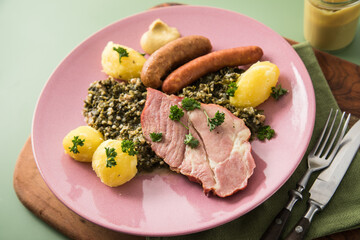 Oldenburger Grünkohl mit geräucherter Kohlwurst, Pinkel, Kassler Nacken, Kartoffeln, Senf, Petersilie auf Holzbrett, Serviette, Teller pink, und grün Hintergrund