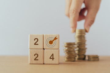 2024 ,dartboard instead of zero on  wood cube block with blurred hand arranging stack of coins. For...