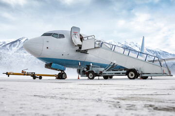 Passenger airliner with air-stairs on the airport apron in a blizzard on the background of high picturesque snow capped mountains