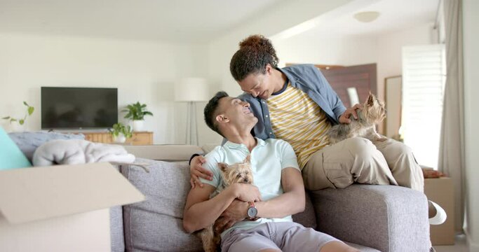 Portrait of happy diverse gay male couple with pet dogs in living room, copy space, slow motion