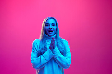 Wow. Surprised, delightful young woman in knitted warm sweater clapping of joy against pink...