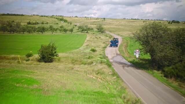 Tractor drives through the fields on a dirt road. Aerial flight over the green land of Germany.