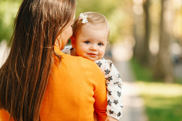 Close up photo of mother holding her baby girl on arms outdoors.