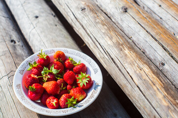 Close-up strawberry crop lying in a plate on rural wooden steps. The concept of healthy food, vitamins, agriculture, market, strawberry sale