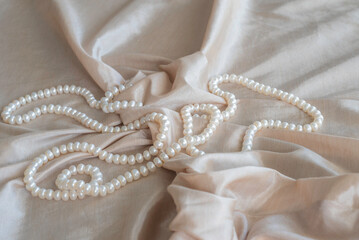 Pearl necklace on silk fabric background.
