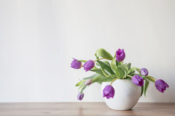 purple tulips in white ceramic vase on wooden shelf