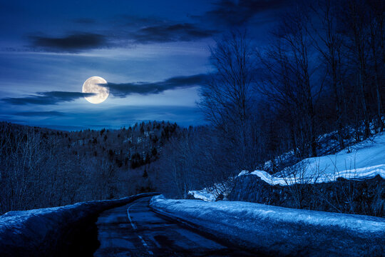 pass with snow on the roadside at night. mountainous winter landscape with forested hills in full moon light