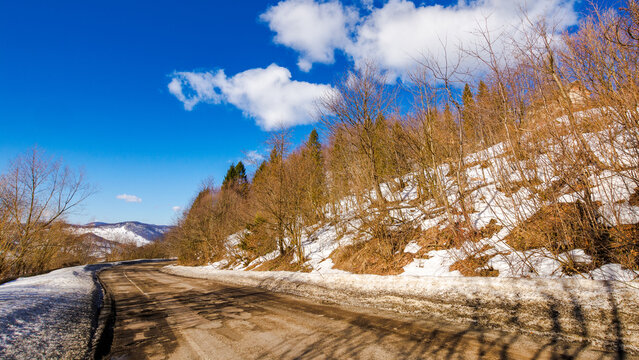 old road pass through snow covered hills. mountainous winter landscape on a sunny day beneath a blue sky with clouds