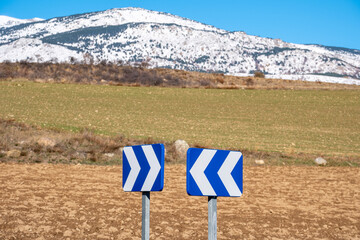 Traffic sign warning of a dangerous curve in a landscape with grasslands and snow-capped mountains