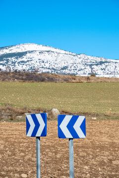 Traffic sign warning of a dangerous curve in a landscape with grasslands and snow-capped mountains