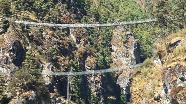 Trekking to Everest Base Camp. Tourists and sherpas with backpacks walk on Hillary suspension bridge through deep rock gorge of Himalayan mountains in Nepal.