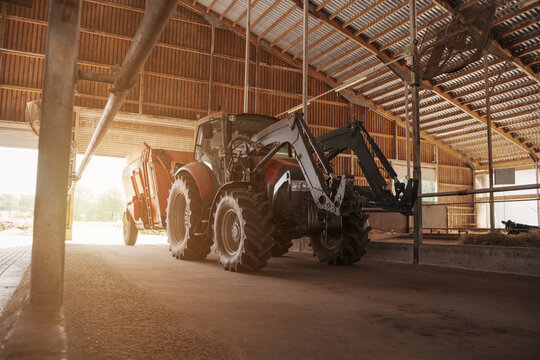 A red and black modern tractor equipped with a loader, parked inside a spacious wooden barn