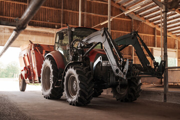 A red and black modern tractor equipped with a loader, parked inside a spacious wooden barn