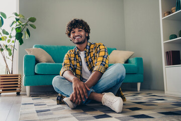 Photo of positive glad nice man freelancer sitting on floor in comfortable flat dorm living room enjoying free time alone indoors